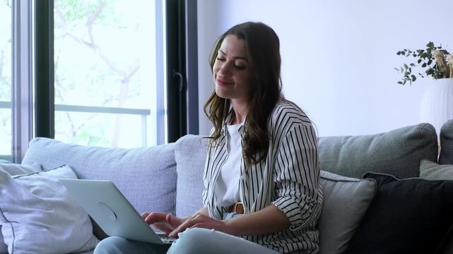 A young woman works efficiently on her laptop from the comfort of her sofa, then closes it and relaxes, embracing a peaceful break. Captures remote work, productivity, and home comfort.