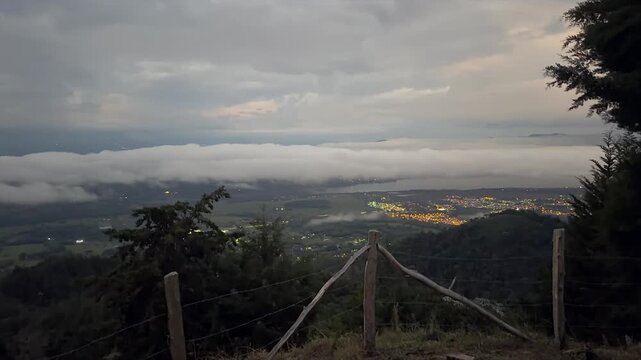 view of city lights and valley under thick fog and clouds at sunrise