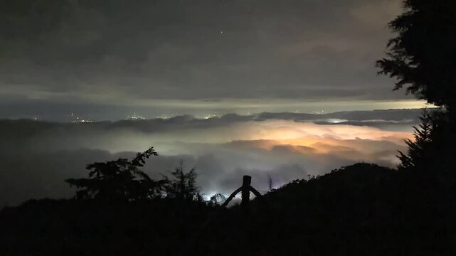 night city lights glowing through fog and mountain clouds