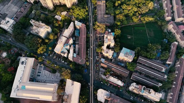 Top-down aerial drone footage of Mumbai, India, showing dense urban buildings, roads, green spaces, residential areas and pockets of agricultural land in warm golden-hour light.