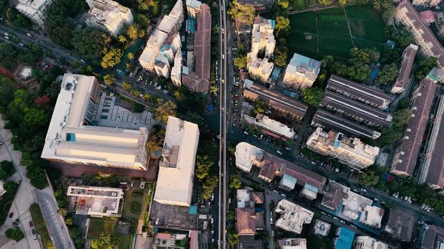 Top-down aerial drone footage of Mumbai, India, showing dense urban buildings, roads, green spaces, residential areas and pockets of agricultural land in warm golden-hour light.