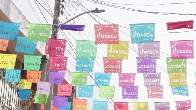 Festive multicolored papel picado banners with the name huasca waving in the wind in a street