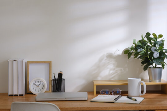Clean modern desk setup with laptop, stationery, clock, coffee cup and indoor plant in soft natural light, ideal for remote work them