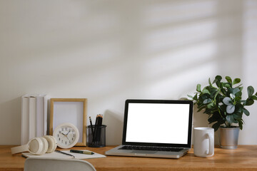 Fototapeta premium Modern home office workspace with laptop mockup screen, calculator, notebook, headphones, coffee cup and stationery on wooden desk.