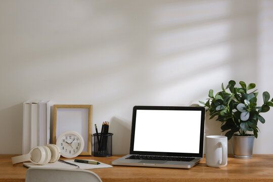 Modern home office workspace with laptop mockup screen, calculator, notebook, headphones, coffee cup and stationery on wooden desk.