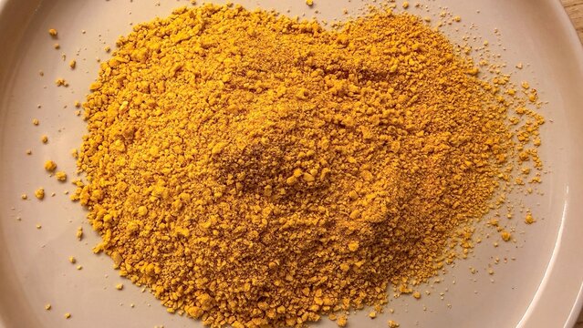 Close up view of bright yellow turmeric powder piled on a plain ceramic plate, suggesting culinary use or natural remedy ingredients, vibrant earthy tones