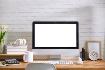 Fototapeta premium Modern office desk setup with desktop computer mockup, keyboard, mouse, calculator, coffee mug and stationery on a wooden table against a white brick wall.