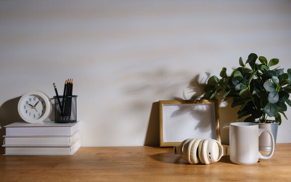 Minimal home office still life with books, clock, pencils, headphones, coffee mug and green plant arranged on a wooden desk with copy space.