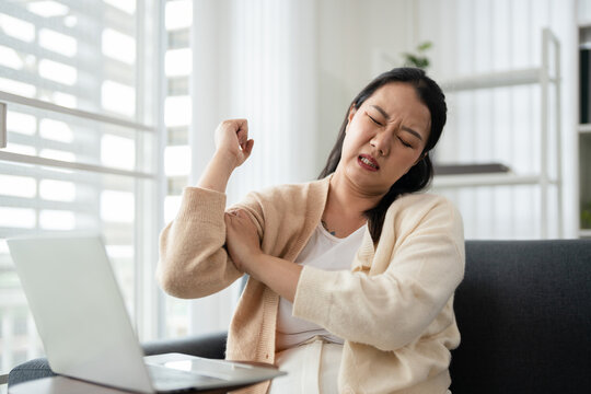 Woman suffering from arm and shoulder ache after working with laptop computer in bad posture.