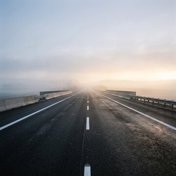 Asphalt highway bridge stretching into heavy morning fog with soft sunrise light