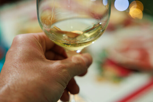 mano di ragazzo adulto caucasico che regge un calice con del vino bianco