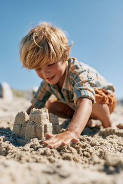 Blonder Junge baut konzentriert Sandburg am sonnigen Strand