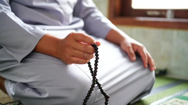 Close-up of hands reciting dhikr using prayer beads. Hands reciting dhikr. A man reciting dhikr while holding prayer beads. A Muslim's worship activity.
