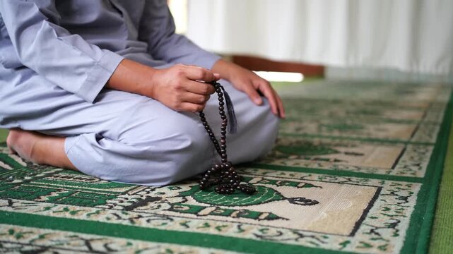 A close-up photo of a hand performing dhikr with prayer beads inside a mosque. A hand engaged in dhikr. A man performing dhikr while holding prayer beads. side shot
