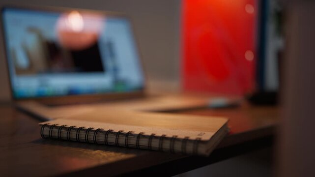 Close-up of prescription eyeglasses resting on a notebook while a laptop works in background. Female hands pick up glasses, illustrating vision care, eye health and screen use.