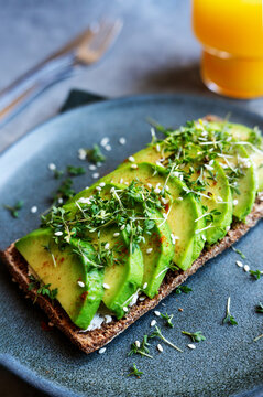 Close-up of sliced avocado, sesame seeds, and cress on rye flatbread.