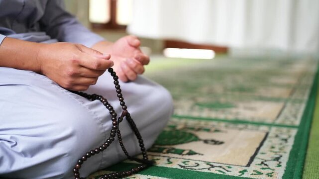 A man holds prayer beads in his hands while reciting dhikr. Close-up of a Muslim man's hands counting prayer beads on a prayer mat. A Muslim's worship
