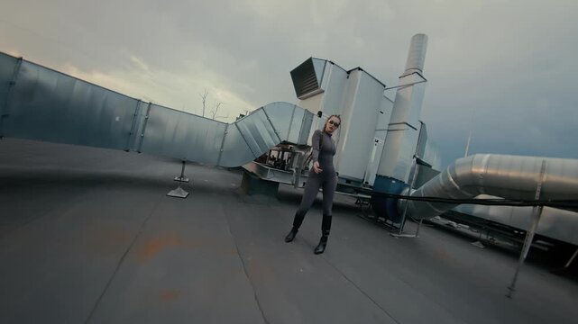 Confident woman posing on rooftop beside industrial ducts under cloudy sky with soft muted lighting