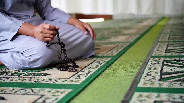 Close-up of hands reciting dhikr using prayer beads against a blurred background. Hands reciting dhikr. A man reciting dhikr while holding a prayer beads. A Muslim's worship activity.

