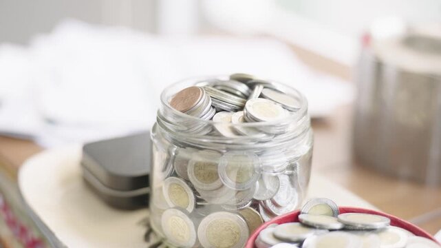 Close up of mexican peso coins collected in a glass jar and a red bowl, representing savings