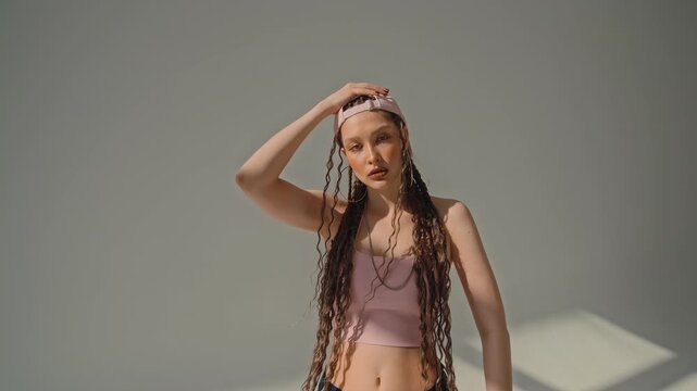 Barefoot woman in pink cap holds dance pose under strong studio light in minimalist gray space room