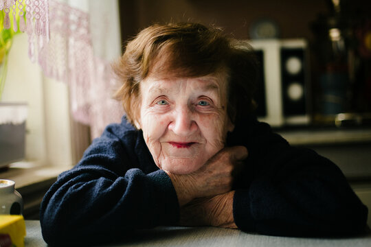 Smiling senior woman resting her arms on a kitchen table at home in warm natural window light