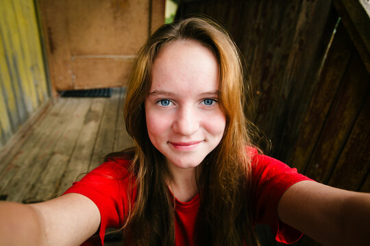 Smiling teenage girl taking a selfie with outstretched arms on a rustic wooden porch