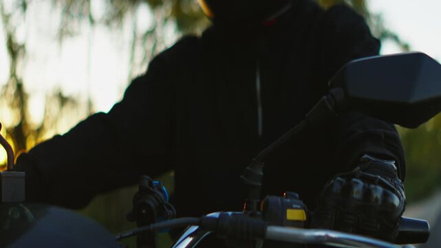 Motorcyclist riding through sunset countryside with bright headlight illuminated and reflective visor helmet capturing warm golden light reflections