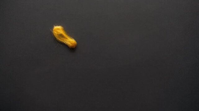 Bright yellow tuft of soft fluffy wool fiber isolated on a dark textured background