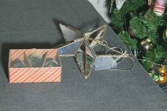 Decorative star and box with ornaments placed on a table near a Christmas tree