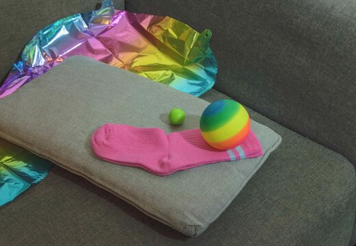 Pink socks and colorful balls resting on a gray couch with shiny fabric nearby in a home setting