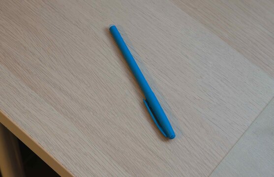 Blue pen placed on a wooden table during daylight hours in a simple workspace setting