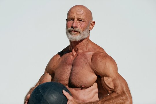 Shirtless senior muscular man posing with a medicine ball against a clear sky for strength poster and workout banner background design