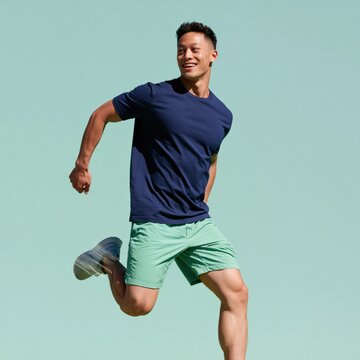 Athletic man mid jump in navy shirt and mint shorts on pastel green background for fitness banner and active lifestyle design
