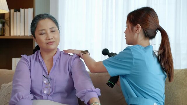 Woman receiving percussive massage treatment on her arm from a caregiver or wellness professional at home, representing muscle recovery, physical therapy, and personal wellness.
