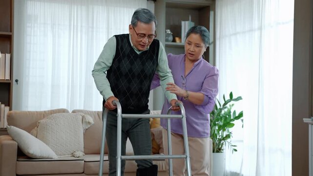 Senior man practicing mobility with a walker while supported by a caregiver at home, representing elderly care, rehabilitation, recovery, and assisted living.
