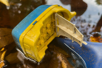 Obraz premium plastic toy boat floating in water puddle on asphalt path with yellow autumn leaves 