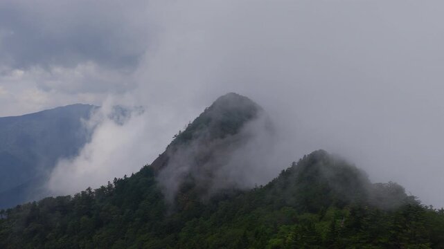 Fog and clouds move over green mountain peak on Shikoku, Japan