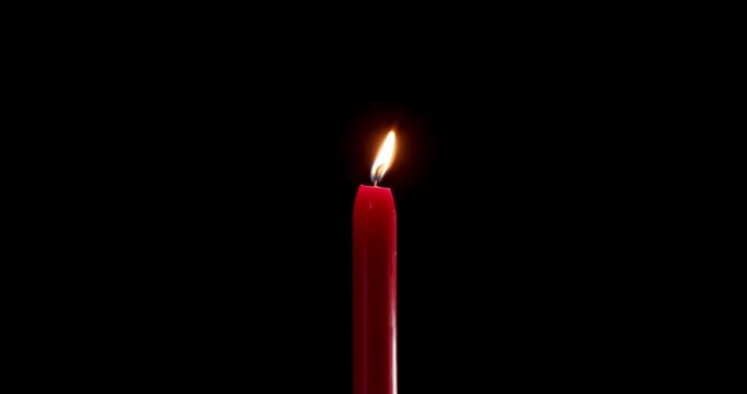 Lit red candle standing alone in a vast and dark space. The moving flame of this beautiful candle creates a mystical atmosphere. A quiet burning candle for soul, prayer, or holiday overlay.
