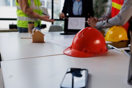 Construction team collaborating on building project, discussing blueprints and property development with safety hardhats on table