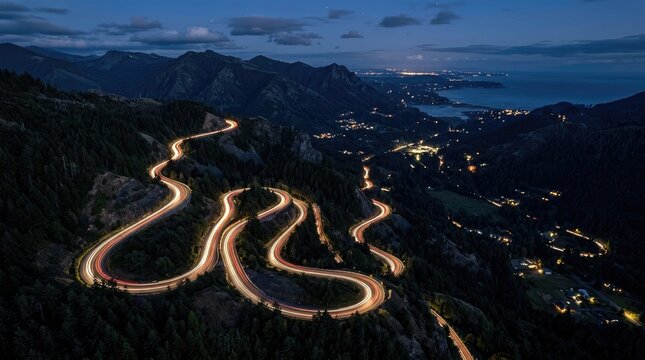 Winding mountain road illuminated at night with city lights in the distance