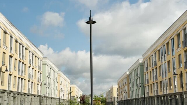 A tall lamppost stands between modern buildings under a cloudy sky. This urban view evokes a calm, peaceful feeling of orderly city life.