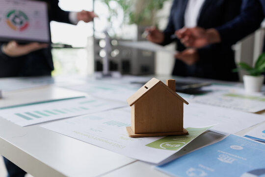 Wooden house model on a table with business people discussing sustainable real estate investment and financial growth