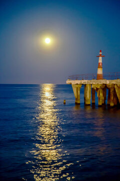 Moonlight path on the sea with a lighthouse at night. Nature, landscape, World tourism.