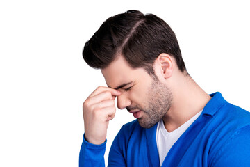 Fototapeta premium Portrait of stylish guy suffering from headache, holding fingers on nose between close eyes, dressed in blue sweater, isolated over grey background