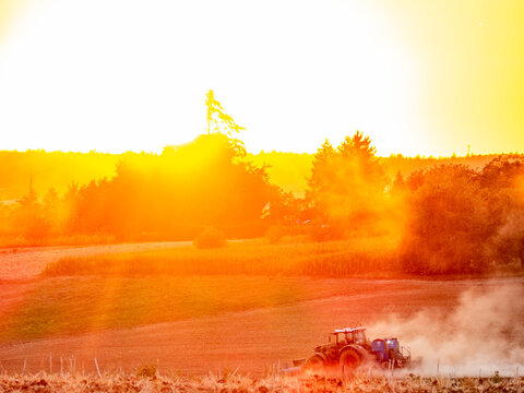 Traktor wirbelt Staub auf bei Sonnenuntergang