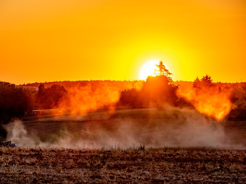 Traktor wirbelt Staub auf bei Sonnenuntergang