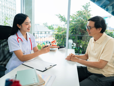 Dentist explaining teeth anatomy to senior patient using human jaw model.