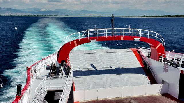 Panoramic view from the ferry deck of the calm sea and mountainous coast, the trail of the ferry against the background of mountains and clouds.