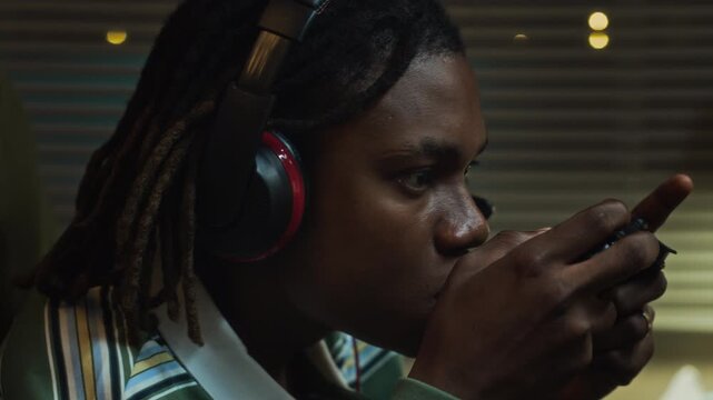 African American teenager eating potato chips while playing video games with controller at night. Clip is ideal for commercial projects on screen addiction, gaming habits, and youth lifestyle